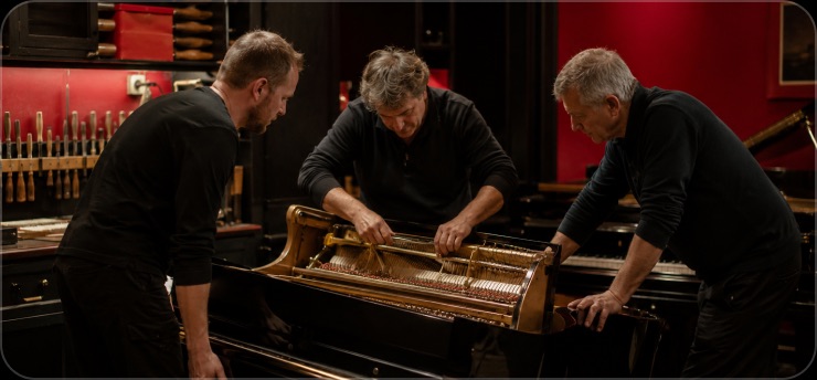 Équipe d'artisans autour d'un piano démonté dans l'atelier